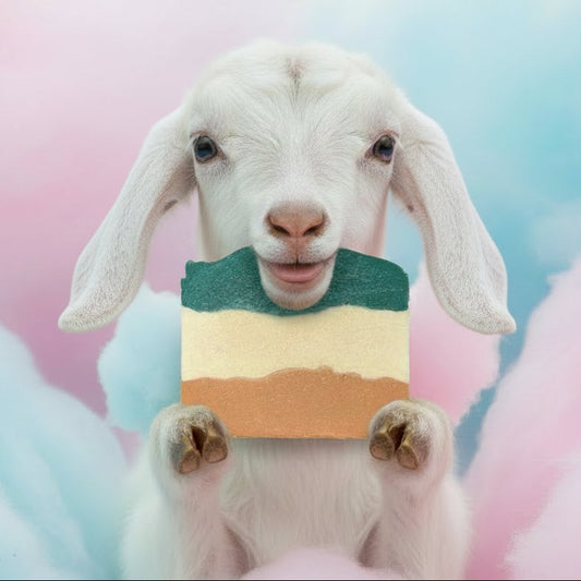 white goat eating/wearing a popsicle goat milk soap color green white and tan stripes against a pastel pink and blue background