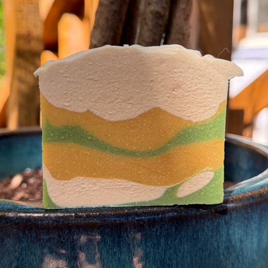 Sage and lemongrass goat milk soap with a Camouflage-pattern of cream green and yellow on a dark surface