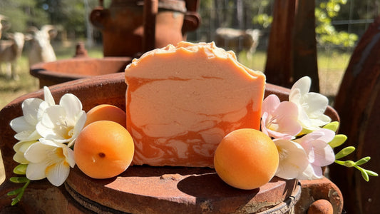 Block of Apricot Freesia goat milk soap with apricots and flowers on a rustic surface outdoors. Apricot color and cream color on soap.