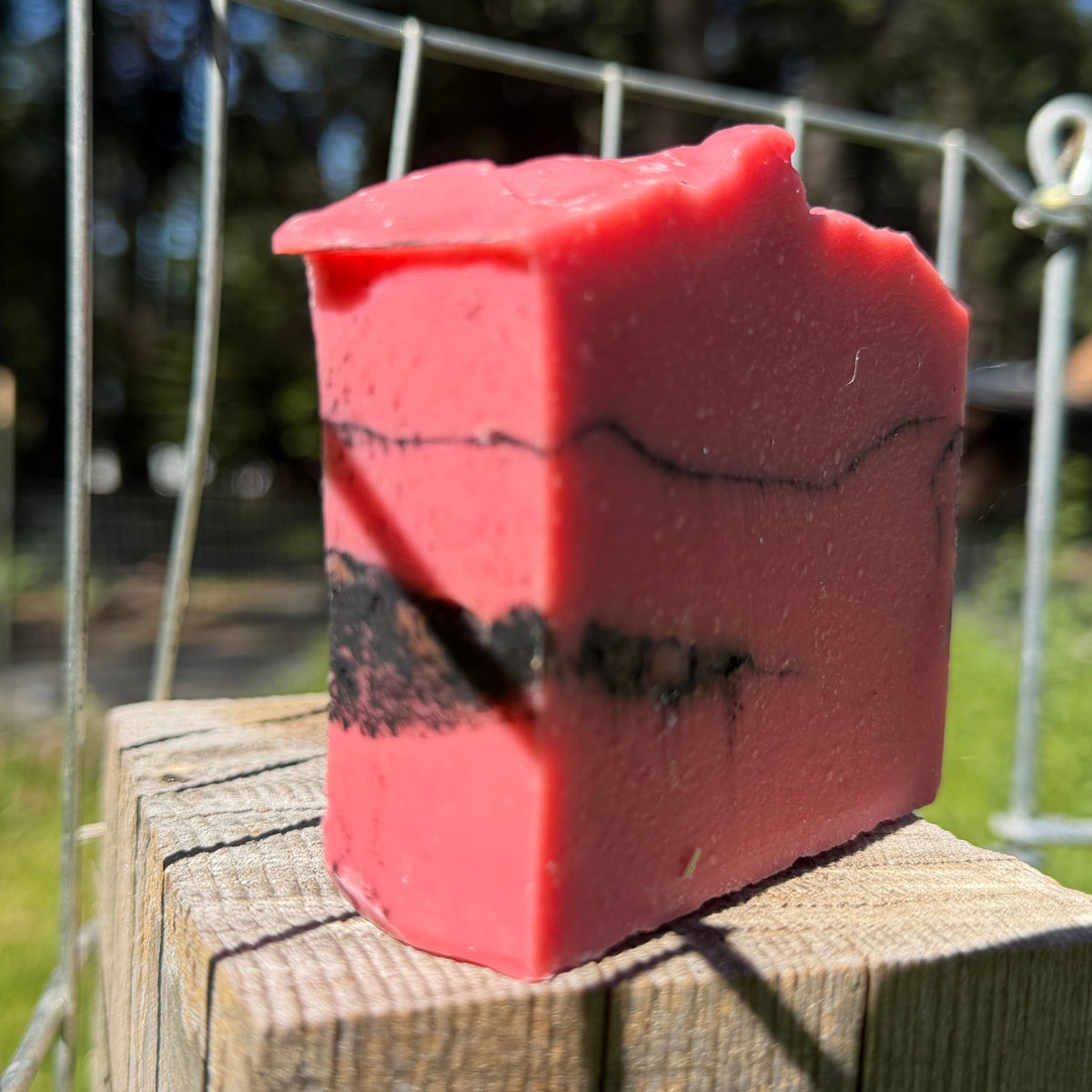 Red soap bar with black accents unscented goat milk  charcoal soap on a wooden block outdoors