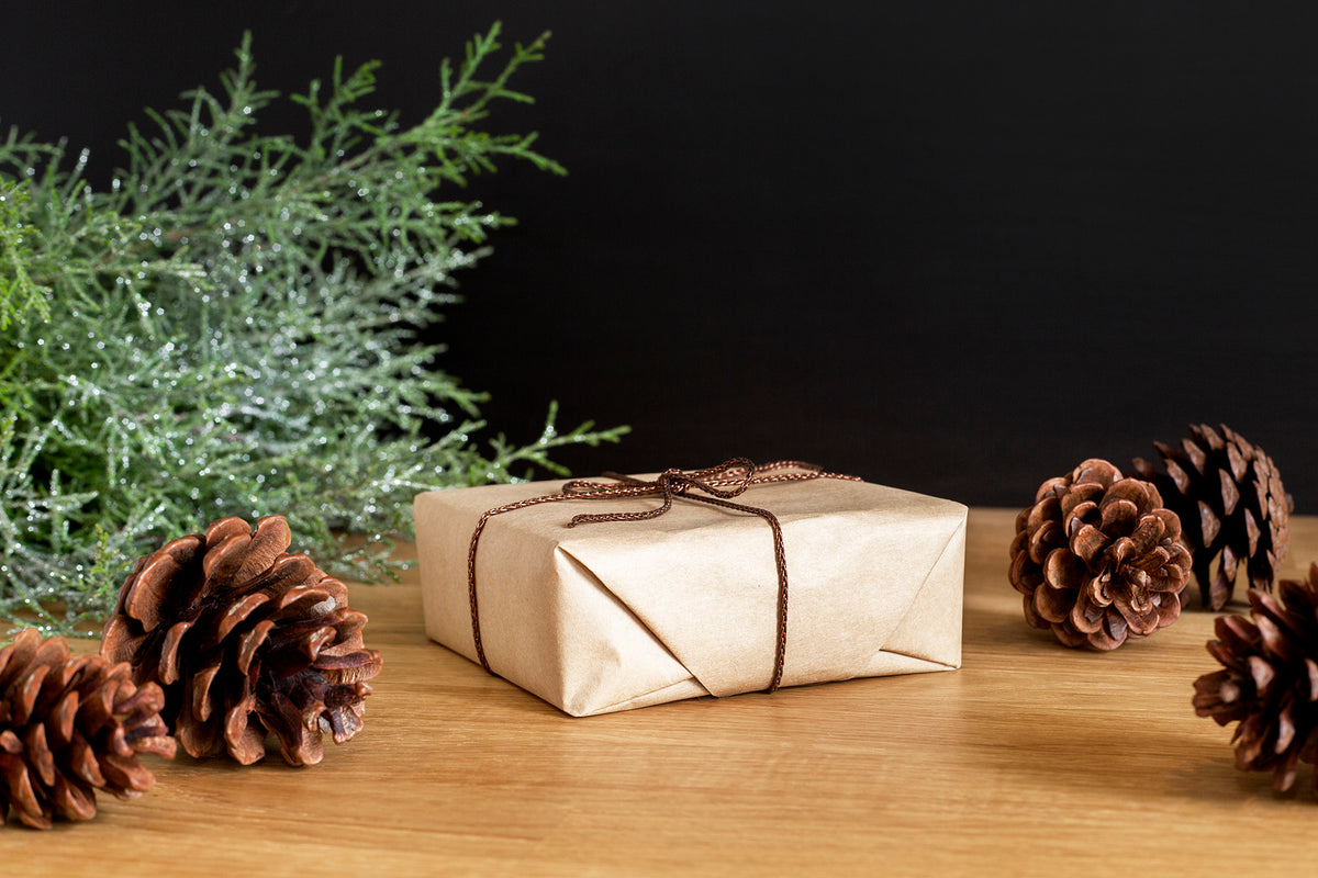 wrapped package with tan wrapping, pine cones and plant branch looks like cedar on a table. with black background.